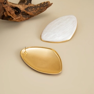 Macro detail of oval geometric stud earrings with white marble texture and gold metal base
