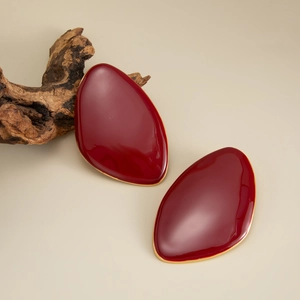 Macro detail of red enamel leaf earrings with elegant gold trim on organic wood background