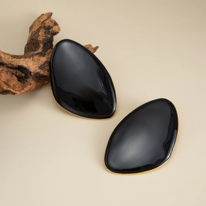 Close-up of black resin gemstone stud earrings with irregular gold pleated metal edges