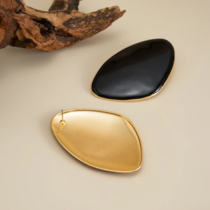 Macro detail of oval black enamel earrings with gold trim and textured metal backing