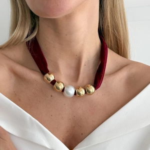 Elegant burgundy velvet choker necklace featuring central pearl and gold beads on a model