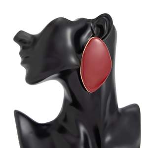 Detailed view of irregular red resin earrings with gold metal edges on a black mannequin