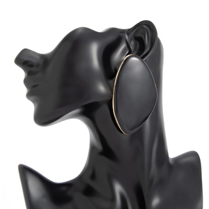 Detail view of large oval black enamel earrings with gold trim on a mannequin bust