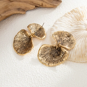 Detailansicht goldener Blütenohrringe mit Struktur auf Naturholz für Vintage-Look