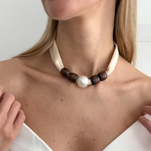 Close-up of bohemian fabric choker with dark wood beads and a large white pearl center
