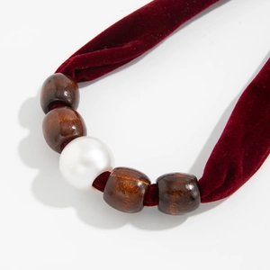Detailed macro view of a red velvet choker featuring a white pearl and brown wooden beads