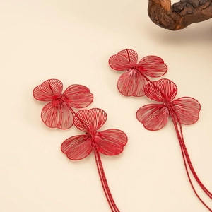 Détail de boucles d'oreilles fleurs rouges avec pétales tressés et longues chaînes à franges