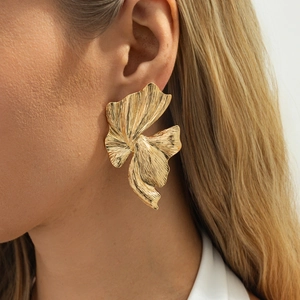 Detail van oversized matgouden bloemblaadjes oorbellen met fijne textuur op model