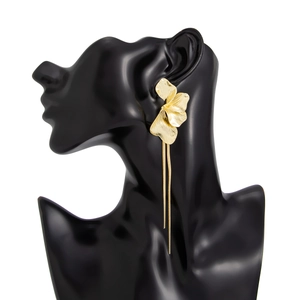 Détail de boucles d'oreilles fleur dorée avec pétales en métal brossé et longs pompons
