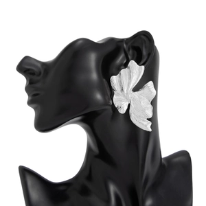 Detail van zilveren metalen blad oorbellen met textuur op een zwarte mannequin