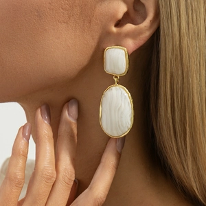 Boucles d'oreilles géométriques en résine avec cadre doré portées par un mannequin sur fond chaud