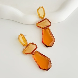 Detail of amber resin geometric earrings with gold claw settings on white wave tray