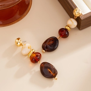 Détail de boucles d'oreilles en résine vintage avec perles ambrées et dorées sur fond beige