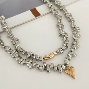 Dettaglio di collana con perle argentate, ciondolo a cuore dorato e ciondoli fluidi