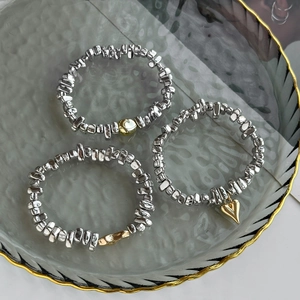 Three-piece irregular silver beaded bracelets with gold heart charms on a glass tray
