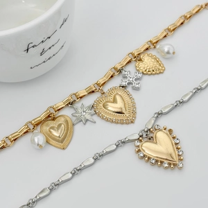Macro shot of gold layered bracelets with textured heart, star, and pearl charms details