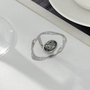 Dettaglio anello in metallo argentato ondulato con cristallo ovale grigio scuro centrale