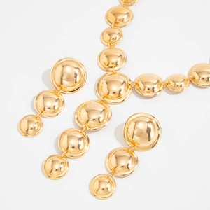 Dettaglio di collana dorata a cupola geometrica e orecchini abbinati con finitura a specchio