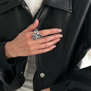 Dettaglio di un anello geometrico argento con tre pietre grigie su un guanto di pelle