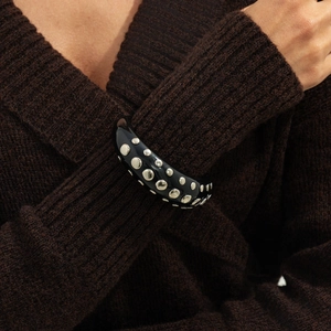 Close-up of wide black resin cuff bracelet with silver studs on a knit sweater background