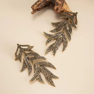 Close-up of vintage gold leaf earrings with micro-paved grey stones on a warm background