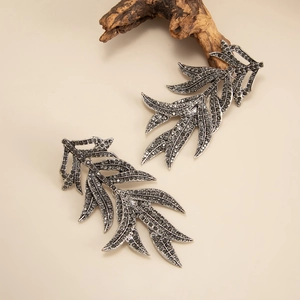 Macro shot of silver-tone leaf earrings with grey rhinestones on a natural branch