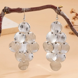 Close-up of silver sequin pendant earrings on wooden branch with textured metal disks