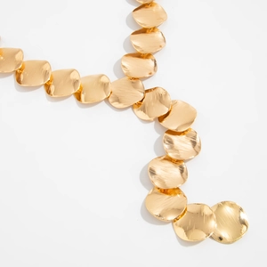Detail of gold Y-shaped tassel necklace featuring brushed metal disc textures