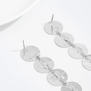 Macro detail of silver geometric disc drop earrings with textured surface and stud backing