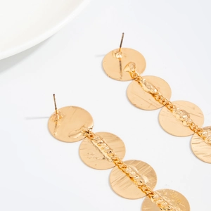 Macro detail of golden metal disc tassel earrings with a brushed texture finish
