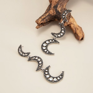 Macro shot of silver crescent moon earrings with black and white crystals on wood