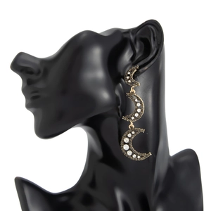 Détail de longues boucles d'oreilles dorées avec triple croissant et micro-pavage de cristaux