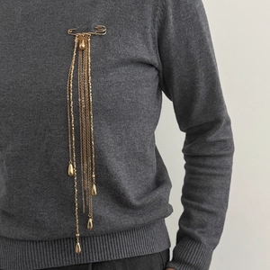 Détail d'une broche dorée à pampilles avec chaînes et pendentifs goutte sur un pull-over