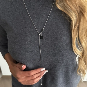 Detail van zilveren Y-vormige lange ketting met zwarte vierkante hanger op grijs