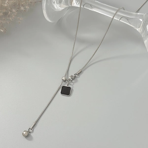 Detail van de zilveren slangenketting met zwarte vierkante hanger en metalen kraal