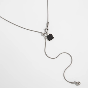 Close-up van verstelbare zilveren slangenketting met zwarte vierkante hanger op witte basis