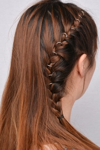 Detailed view of silver metal dreadlock rings intertwined in a fishtail braid style