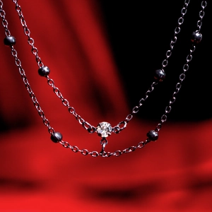 Vista macro di una collana doppia in argento con perline rotonde e un pendente di diamante lucido