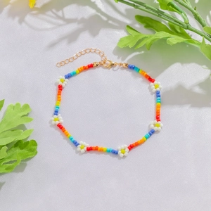Dettaglio di una cavigliera con perline arcobaleno, fiori di margherita e chiusura d'oro