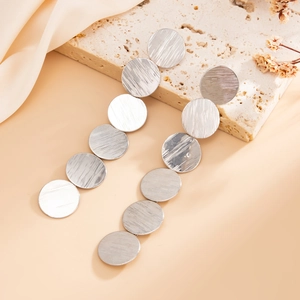 Detail of silver long drop earrings with six brushed metal discs on a stone background