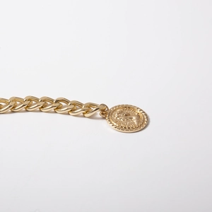 Close-up of vintage gold chunky chain and embossed portrait coin pendant on white surface