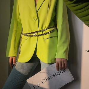Detail shot of a double-layered gold chain belt over a neon green blazer for women