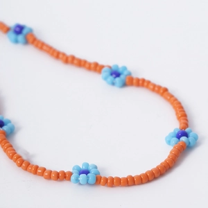Detalle de collar de cuentas naranja hecho a mano con dijes de margaritas azules