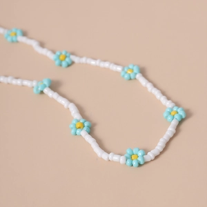 Primer plano de un collar de cuentas blancas hecho a mano con margaritas azules y amarillas