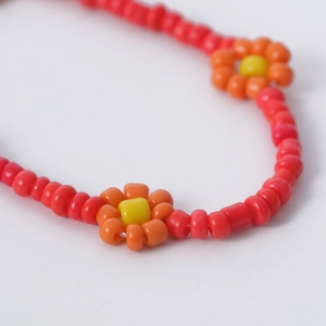Detalle macro del collar de cuentas tejidas a mano con cuentas rojas y patrones de flores naranja
