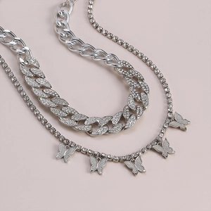 Detalle de cadena cubana plateada y collar tenis con colgantes de mariposas de pavé