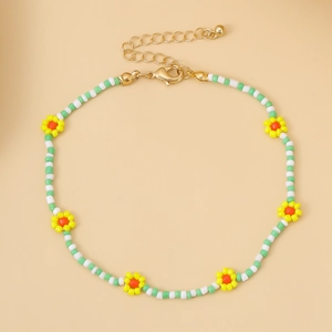 Detalle de collar artesanal de cuentas blancas y verdes con flores amarillas y cierre dorado