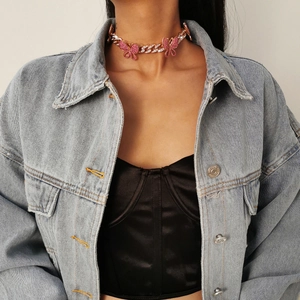 Detail of pink rhinestone butterfly pendants on a chunky Cuban link choker worn by a model