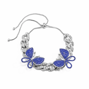 Macro detail of a silver Cuban link anklet with blue rhinestone butterfly and bolo clasp