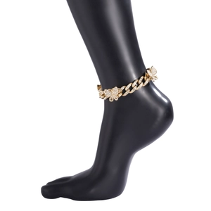 Close-up of gold Cuban link anklet with diamond-studded butterfly charms on a model foot